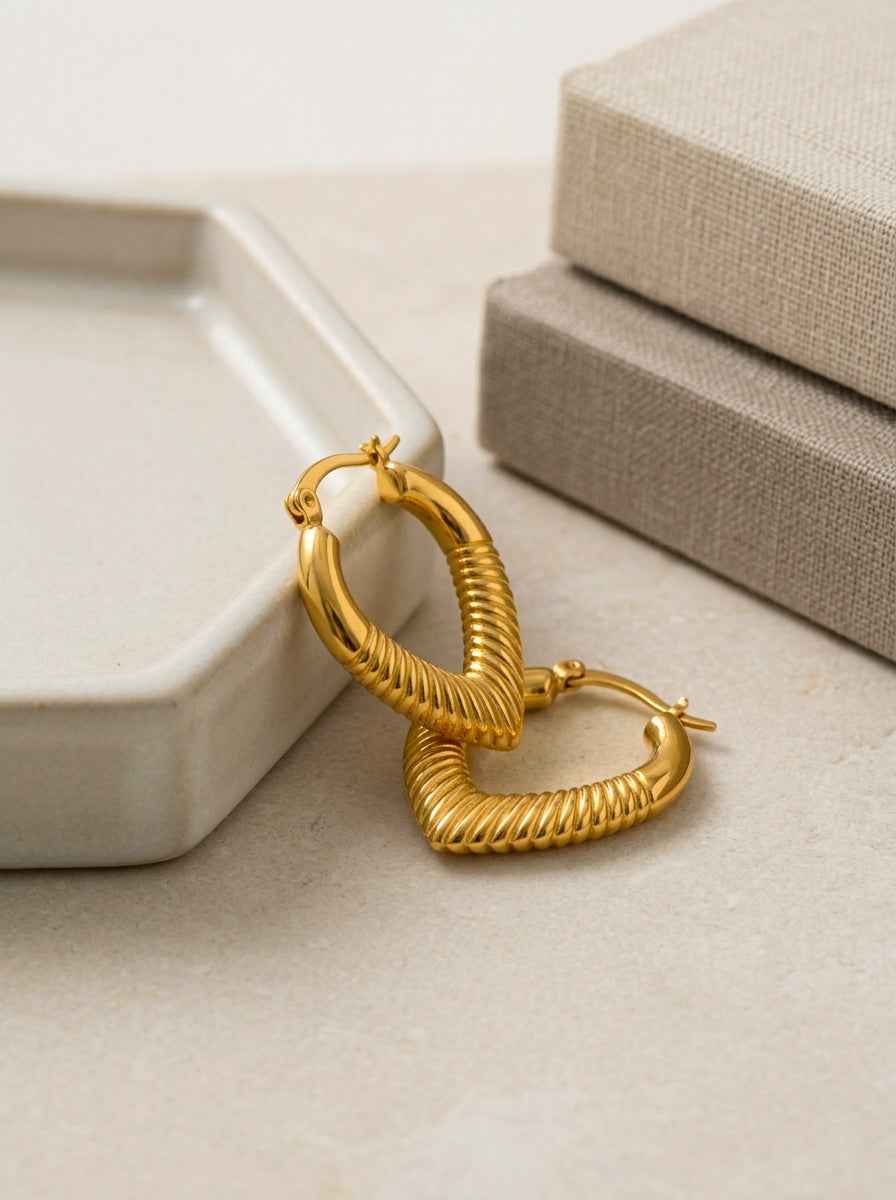 Gold heart hoop earrings on a beige surface with a neutral background