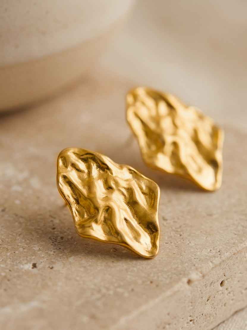 Gold leaf-shaped irregular earrings on a beige surface