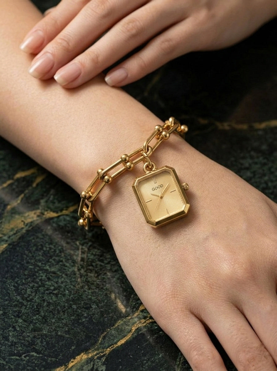 Gold linkage statement watch bracelet on a wrist against a dark marble background