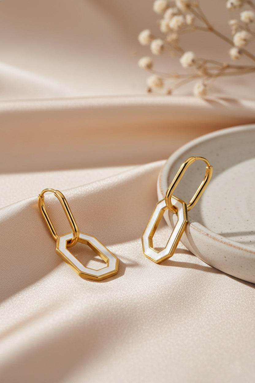 18k Gold drop earrings in hexagon shape on a soft beige surface with dried flowers in the background