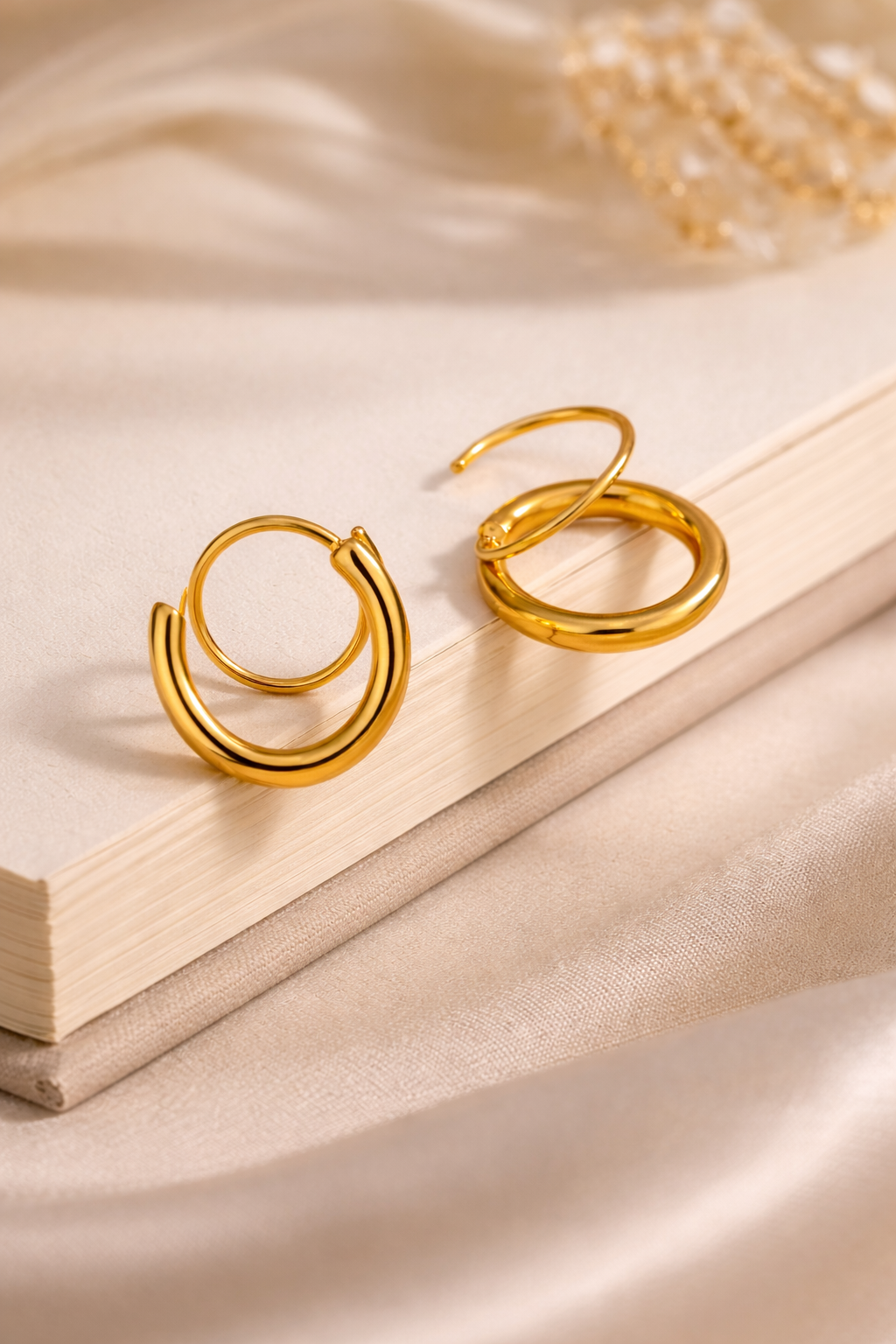 close up of 18k gold double hoop earrings on a beige fabric background