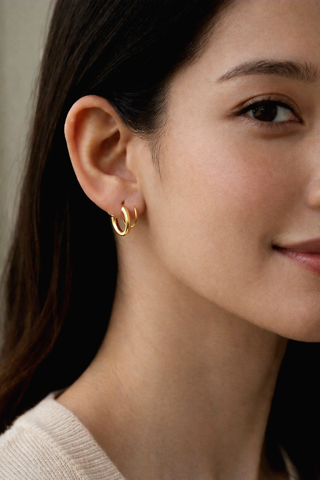 Close-up of a woman wearing stainless steel gold double hoop earrings with a neutral background 