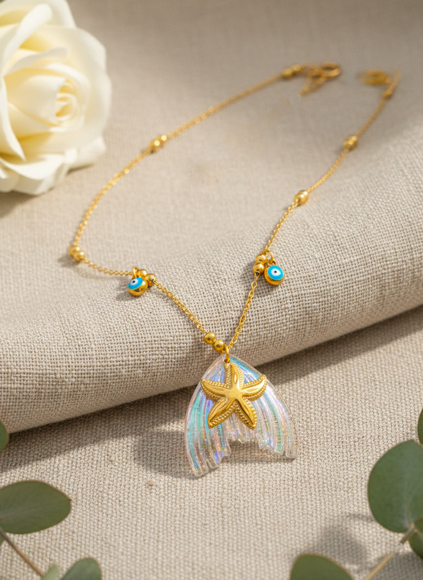 ocean inspired Gold star necklace with a starfish pendant on a textured surface with a white rose and green leaves.
