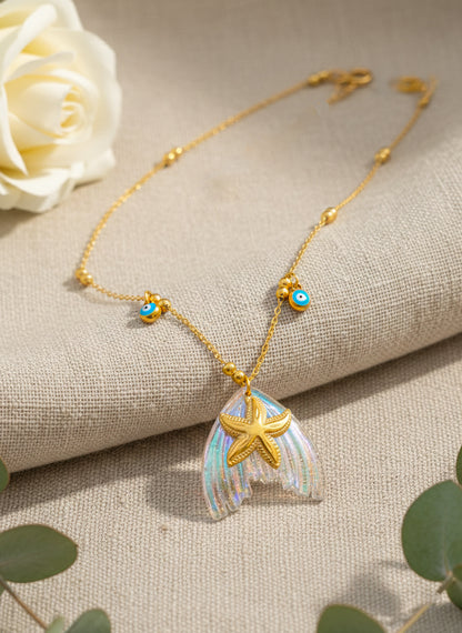ocean inspired Gold star necklace with a starfish pendant on a textured surface with a white rose and green leaves.