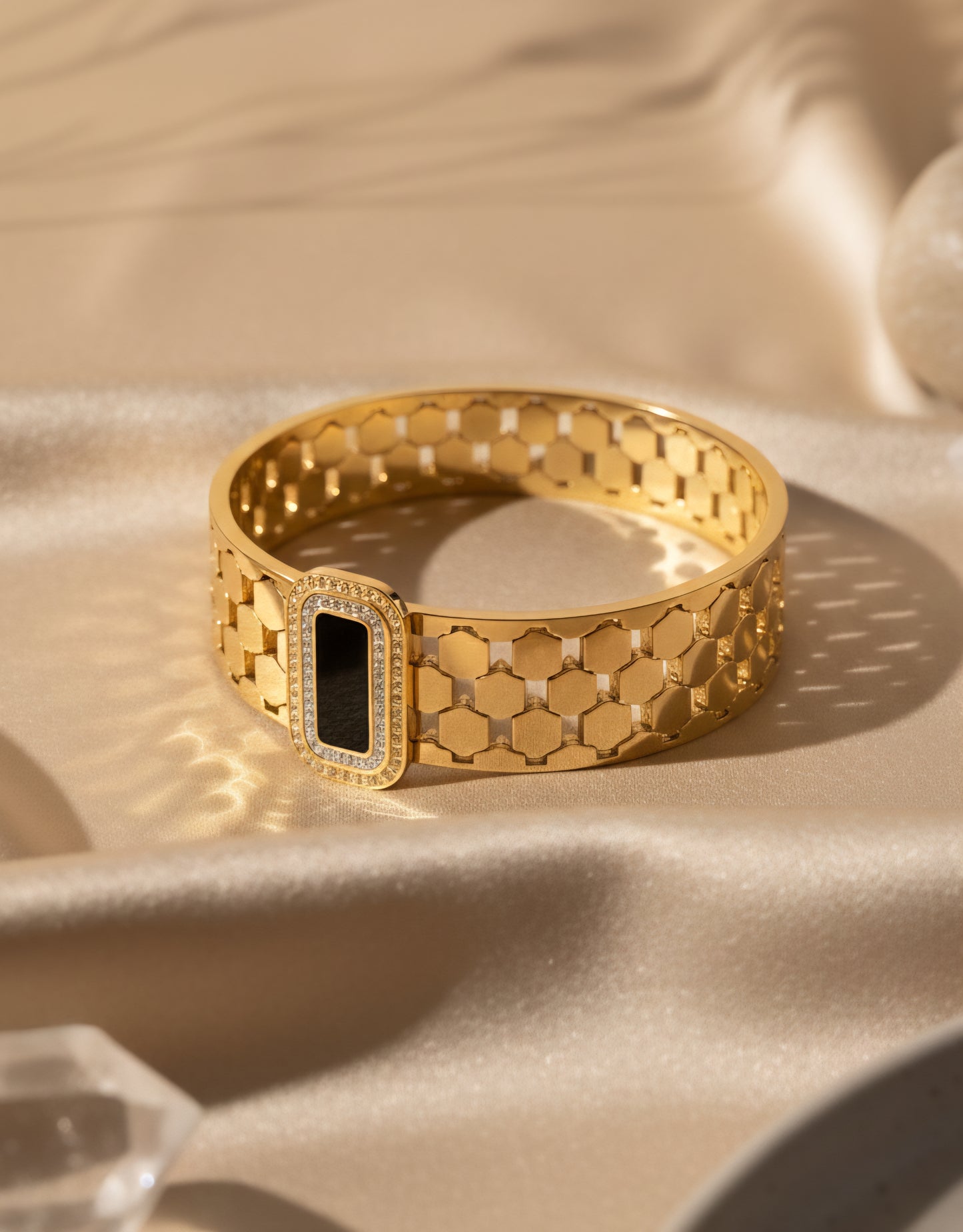 stainless steel Gold bracelet with hexagonal pattern and black stone in centre on a beige fabric background