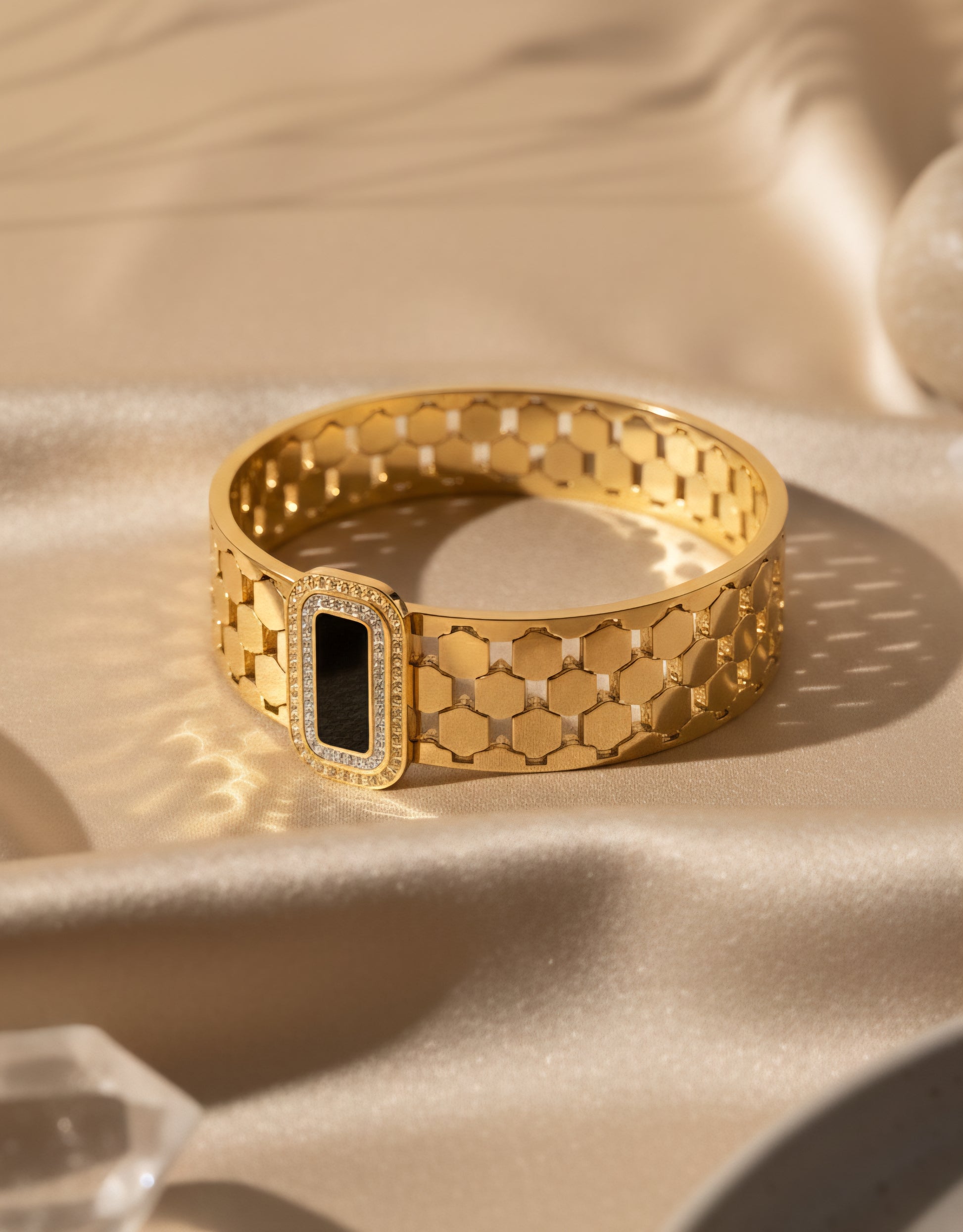 stainless steel Gold bracelet with hexagonal pattern and black stone in centre on a beige fabric background