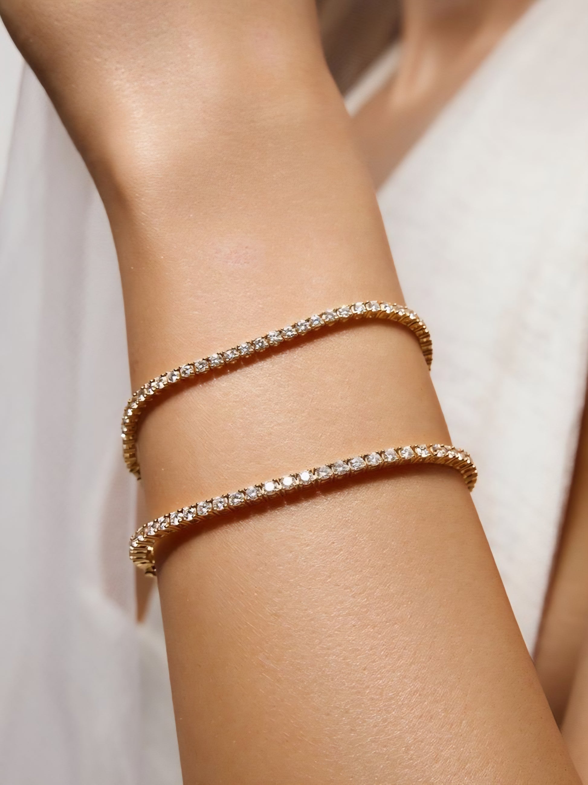 Gold tennis bracelet with clear stones on a person's wrist against a white background