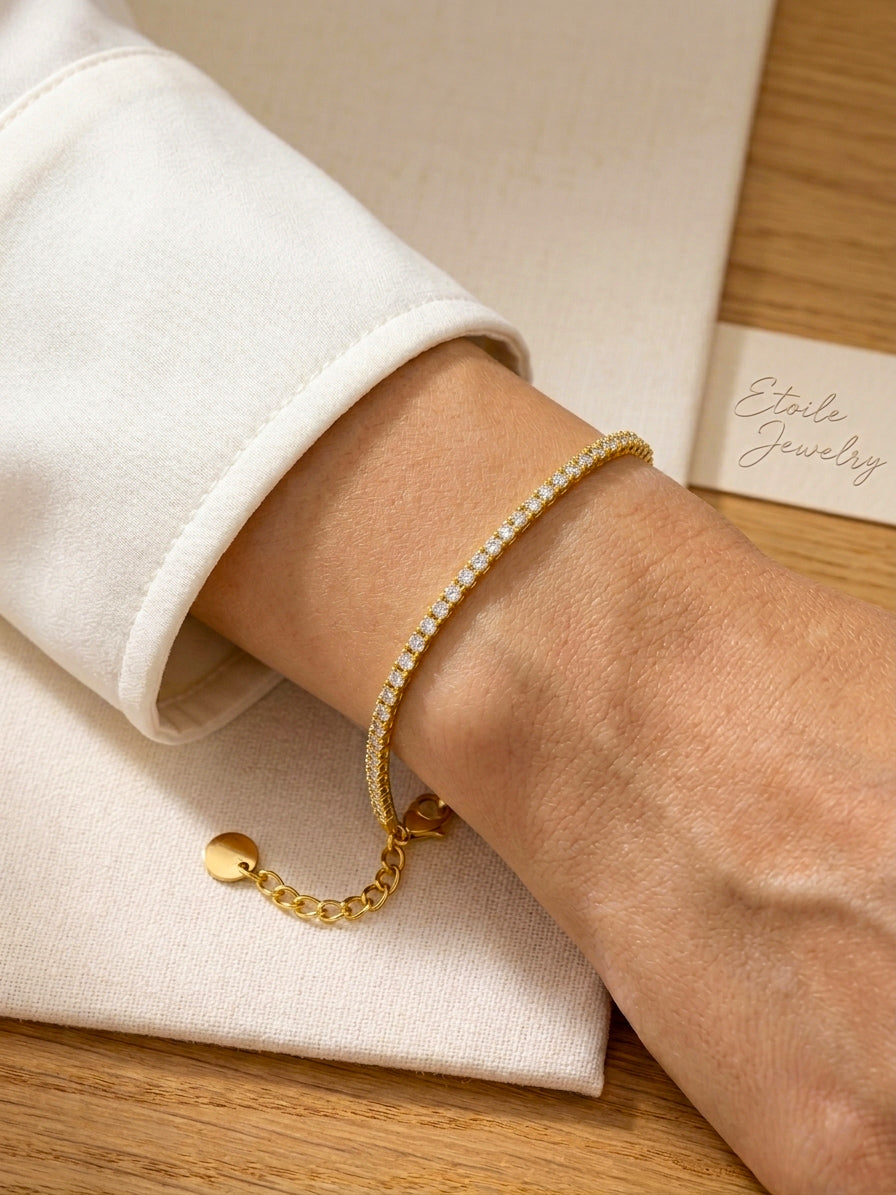 Gold thin tennis bracelet on a wrist with a neutral background