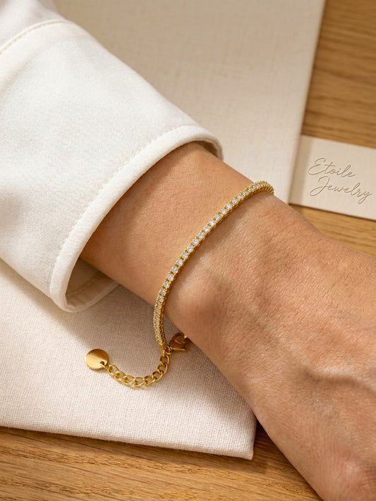Gold thin tennis bracelet on a wrist with a neutral background