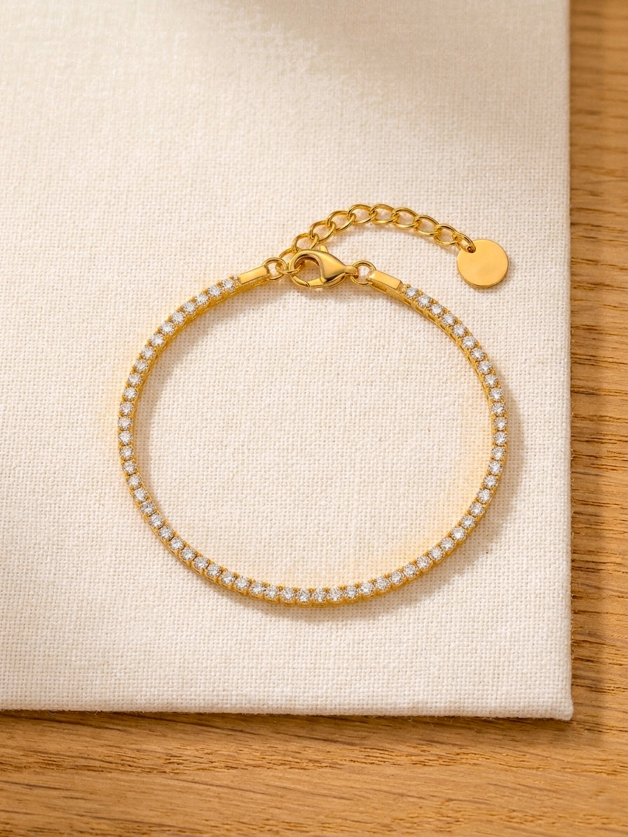 Close up of Gold tennis bracelet with clear stones on a beige fabric background